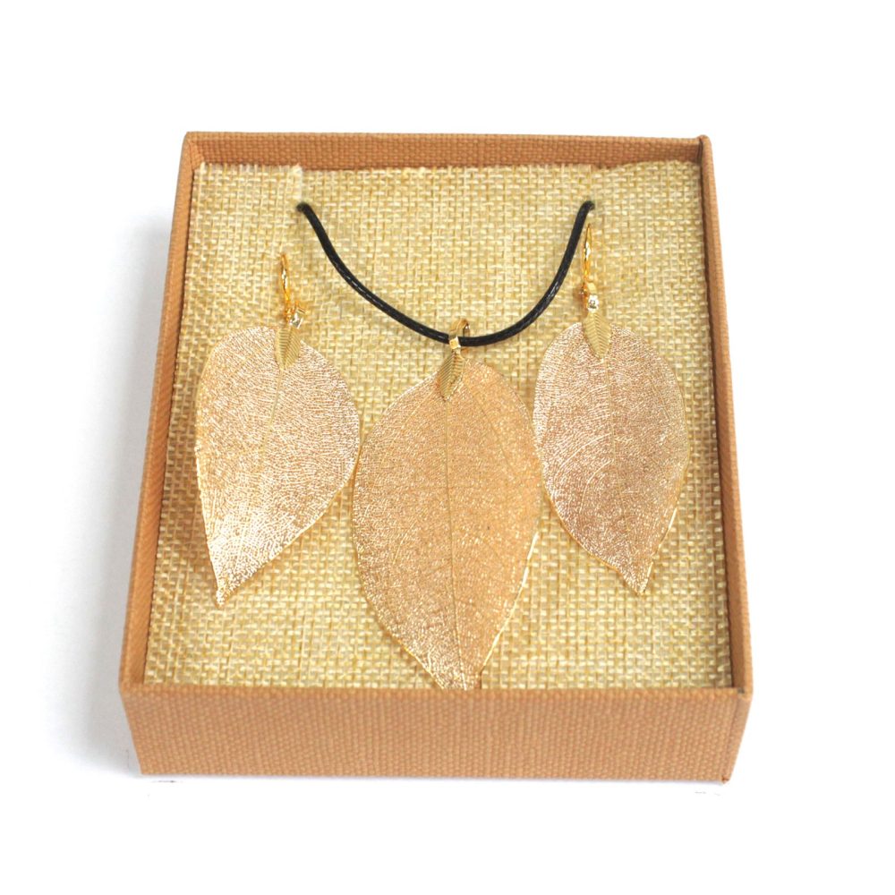Gold-colored leaf earrings and a necklace are displayed in a brown cardboard box with a burlap-textured insert, against a white backdrop.