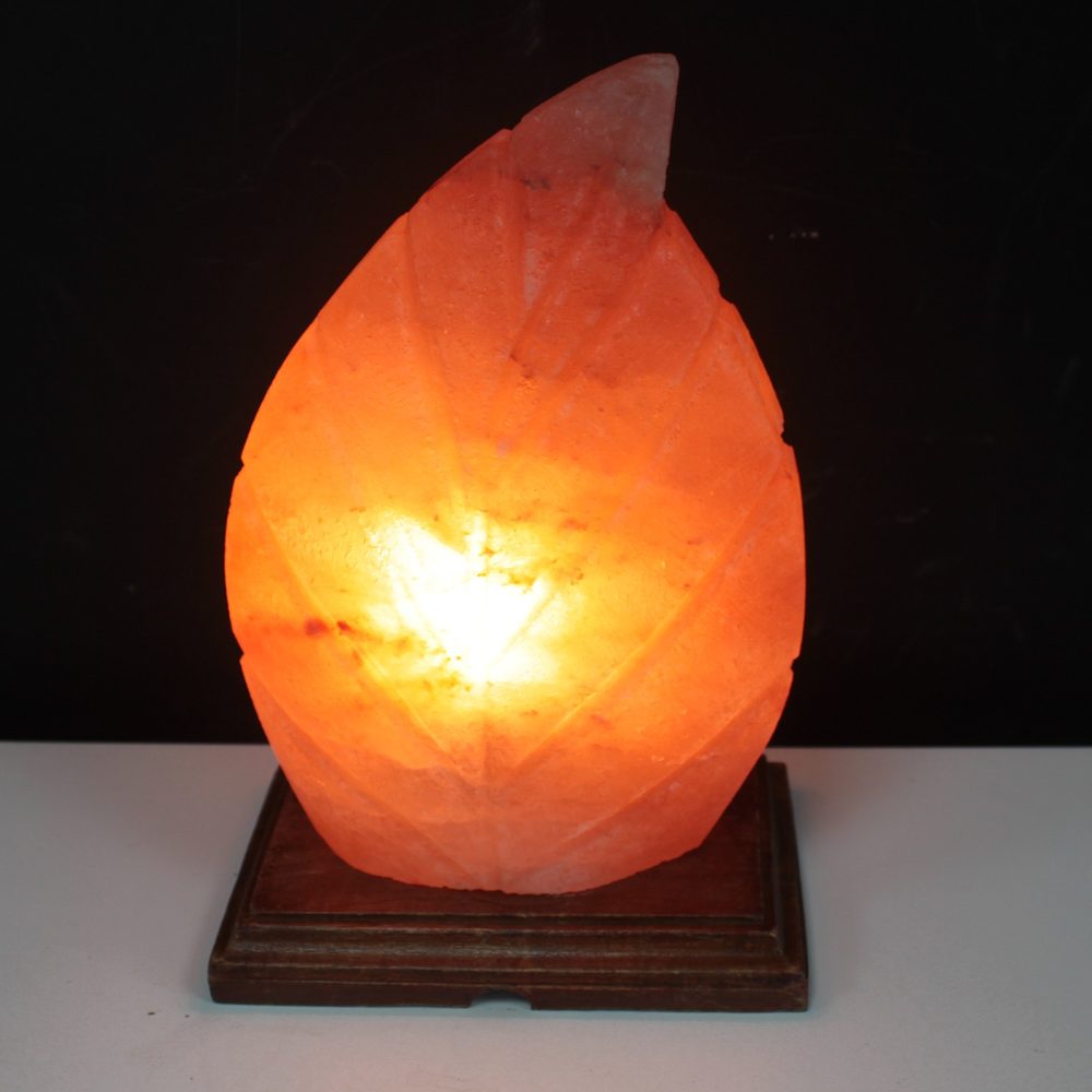A glowing, leaf-shaped orange salt lamp emits warm light, resting on a dark wooden base against a black background.
