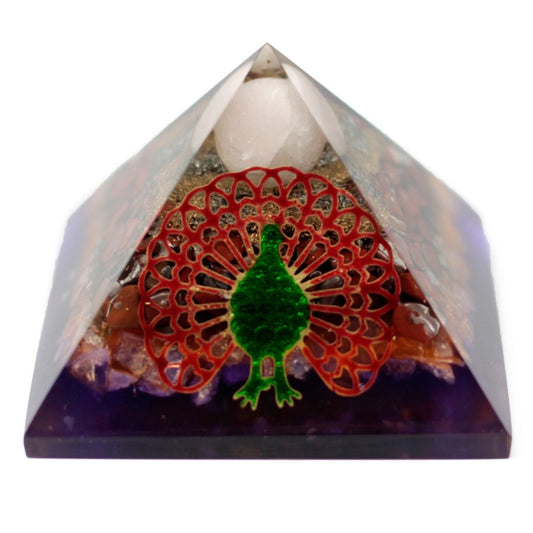 A translucent pyramid encases layers of amethyst, red stone, and gold-colored sand. Inside, a green and red peacock decoration faces the viewer. The top is capped by a white stone.