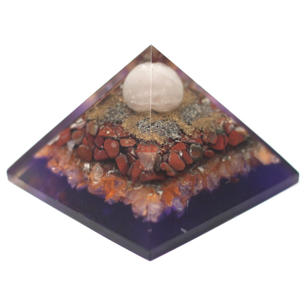 A pyramid shape, constructed from layers of material, has a translucent white orb on top. Layers include crystals, red pebbles, gold dust, and gray material, embedded in purple resin.