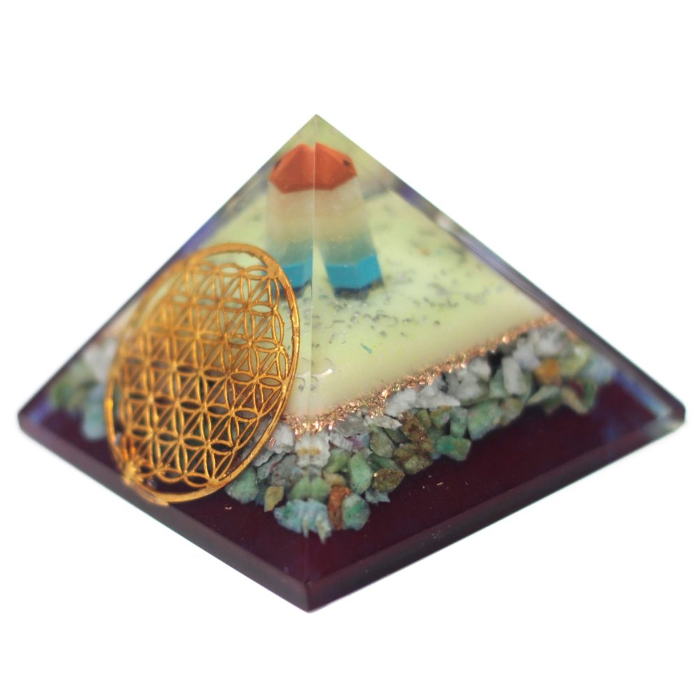 A pyramid rests in isolation, showing a decorative golden flower of life embellishment on one side, along with multicolored stones and a central, segmented crystal enclosed within the resin.