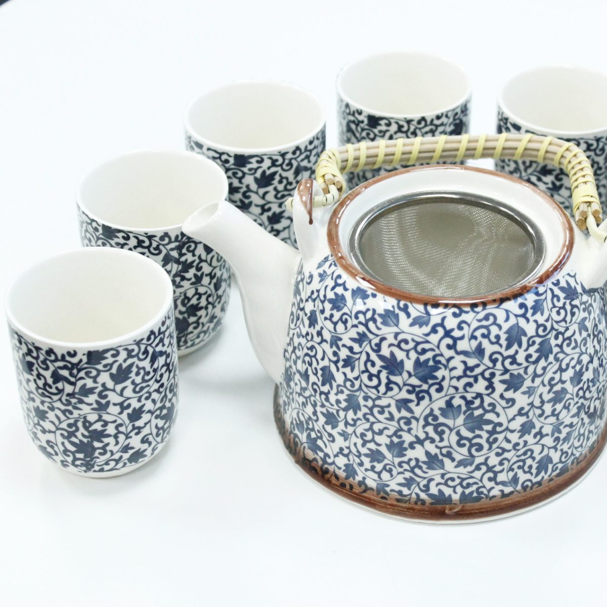A ceramic teapot with a woven handle displays a blue floral pattern, surrounded by five matching cups on a white surface.