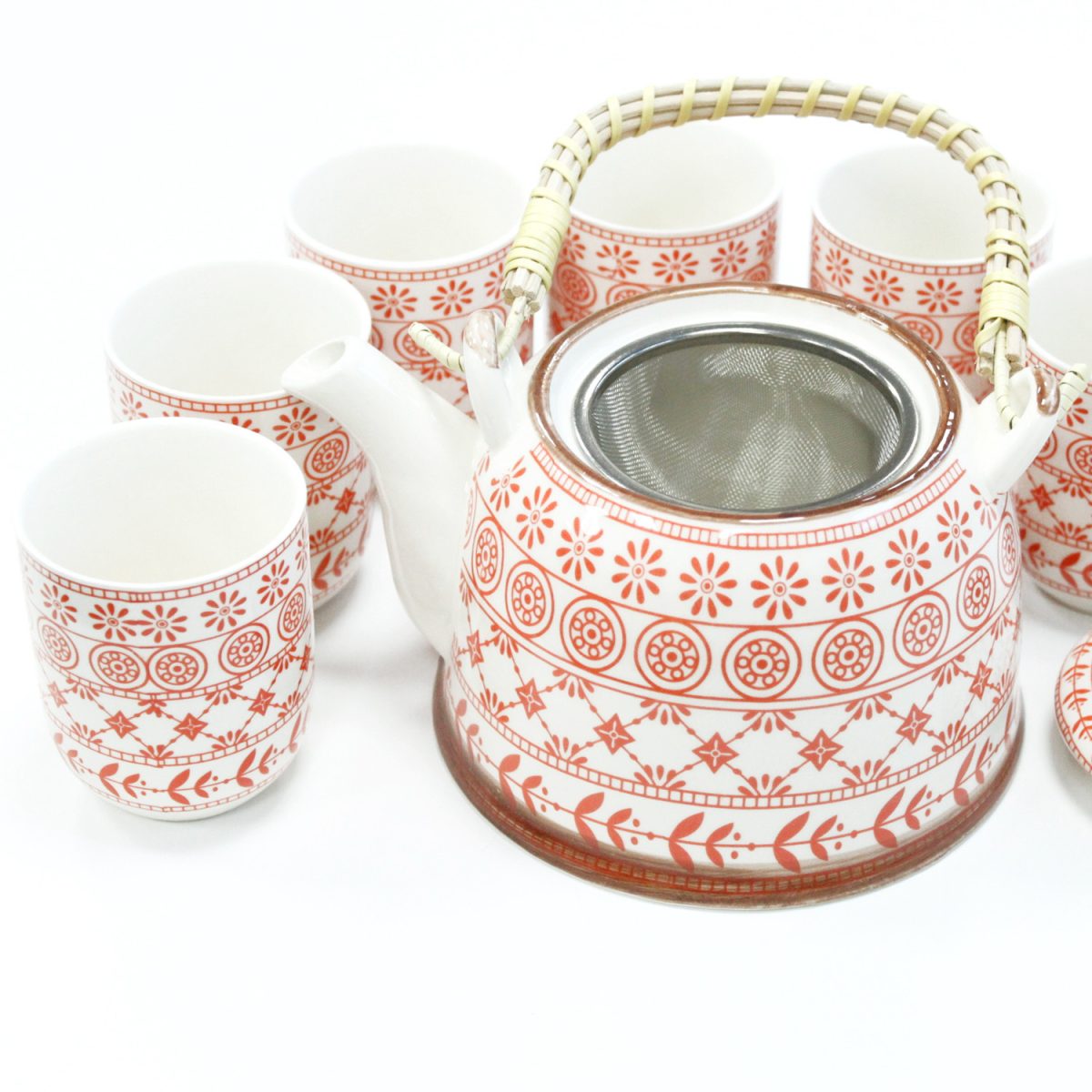 A white ceramic teapot with red floral patterns rests with six matching cups. The teapot has a woven handle and visible metal infuser, placed on a white surface.