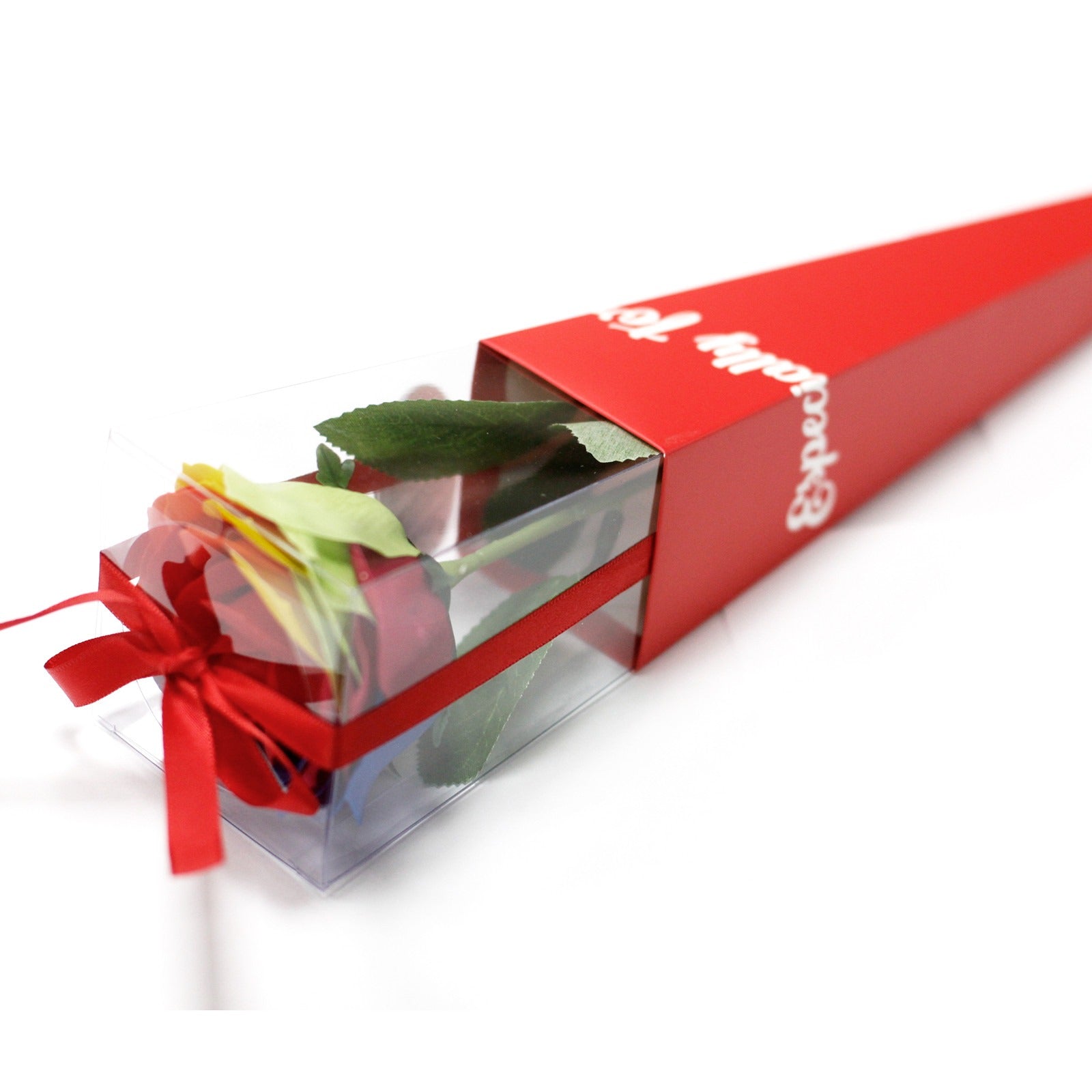 A red rose sits in a clear plastic box with a red ribbon, partially covered by a red box labeled "Especially for". The objects sit on a white surface.