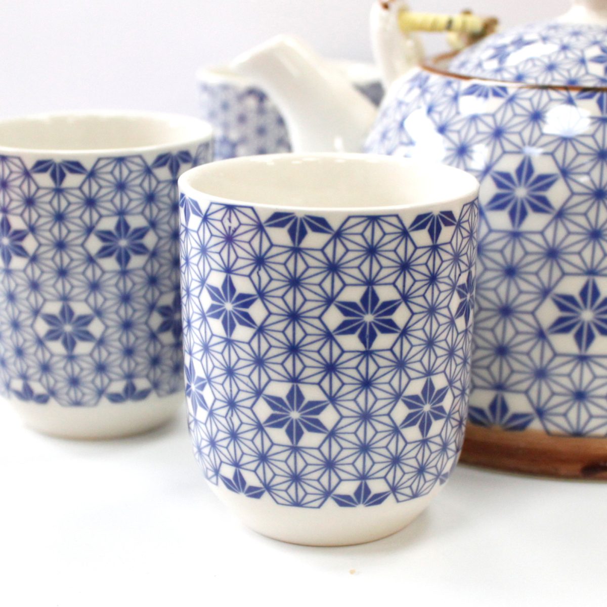 Ceramic teacups with intricate blue geometric patterns are placed alongside a matching teapot. Set on a white surface, the arrangement suggests a coordinated tea set.