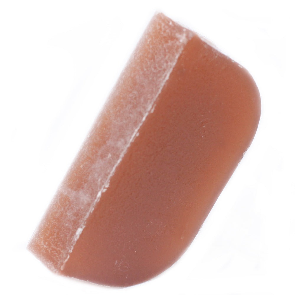 A tan-colored, cube-shaped lozenge sits on a white surface. The lozenge is angled and has one rounded corner.