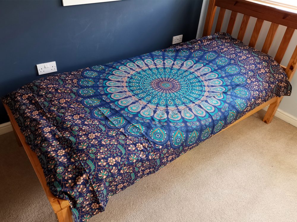 A teal and gold mandala tapestry covers a single bed in a bedroom.