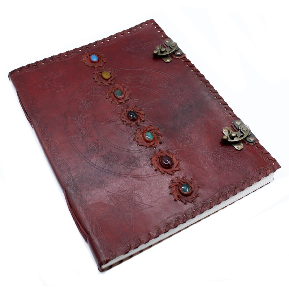 A red leather journal lies closed on a white surface. It features a large star design, gemstones, a braided border, and two metal clasps.