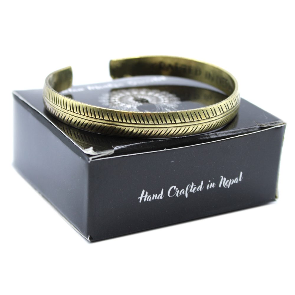 A brass-colored bracelet with incised marks rests on a black box. The box has text that reads “Hand Crafted in Nepal.”