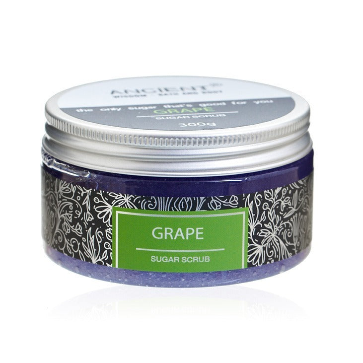 A jar labeled "ANCIENT WISDOM THAT'S GOOD FOR YOU GRAPE SUGAR SCRUB 300g" sits on a white surface. The jar contains grape sugar scrub and has floral designs.
