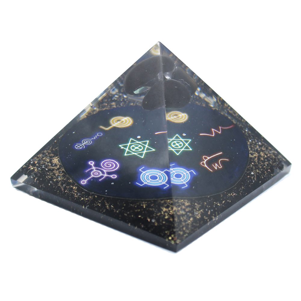 A resin pyramid encases metallic flecks, geometric symbols and black stones. The objects are layered within the clear structure, on a solid white background.