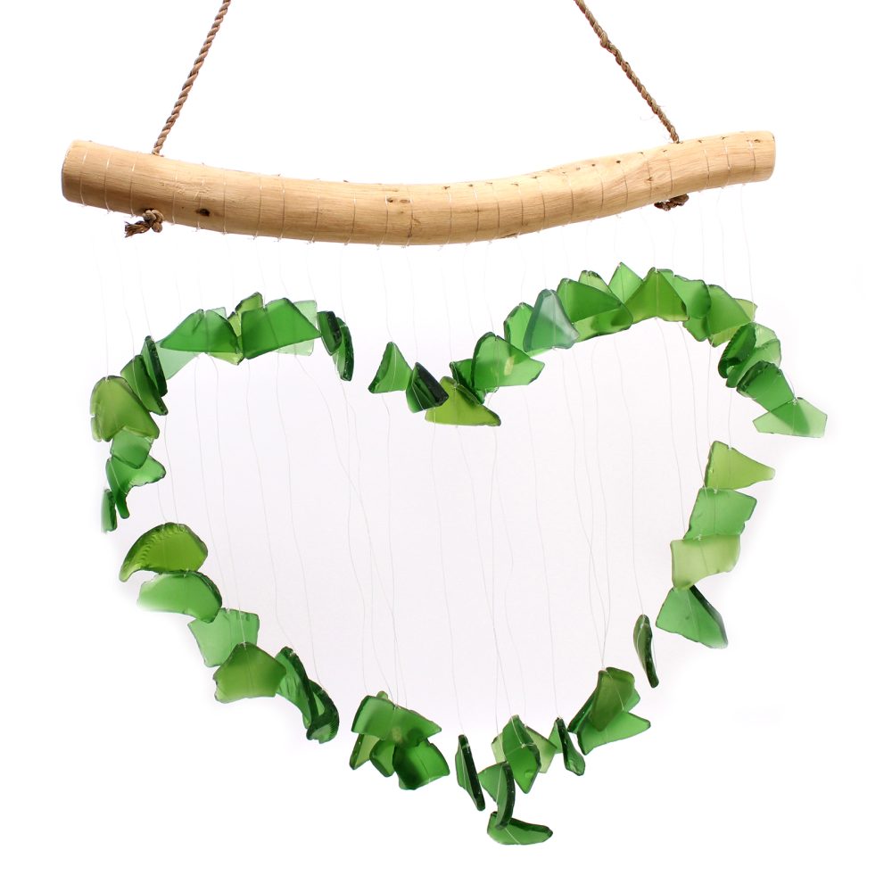 A green glass heart-shaped wind chime hangs from a wooden branch.  The chime gently moves, creating a delicate sound against a white background.