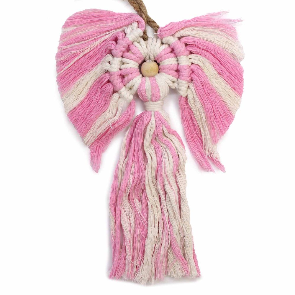 A macrame angel ornament hangs, the decoration in pink and cream. It has a wooden bead at its center, with wings and a tassel. The background is white.