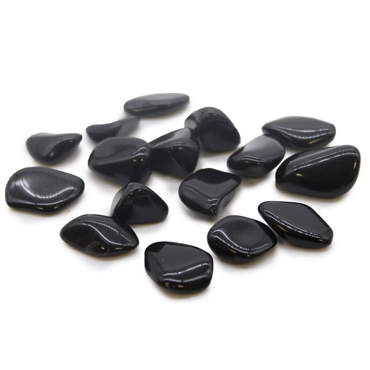 Polished black stones are scattered on a white surface. They are various, rounded shapes.