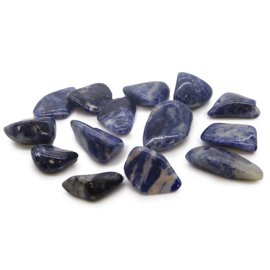 A collection of tumbled sodalite stones are scattered. The blue and white stones are arranged on a white surface.