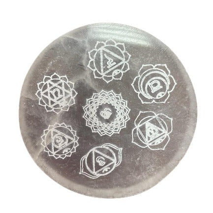 A translucent, circular stone displays seven chakra symbols etched in white. These symbols are arranged in a circular pattern on the stone's surface.