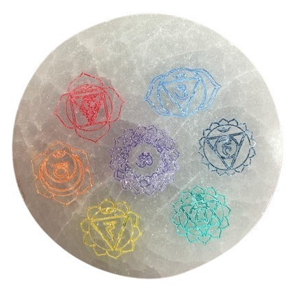 A round, gray selenite disc displays seven chakra symbols arranged in a circle, each in a different color and design.
