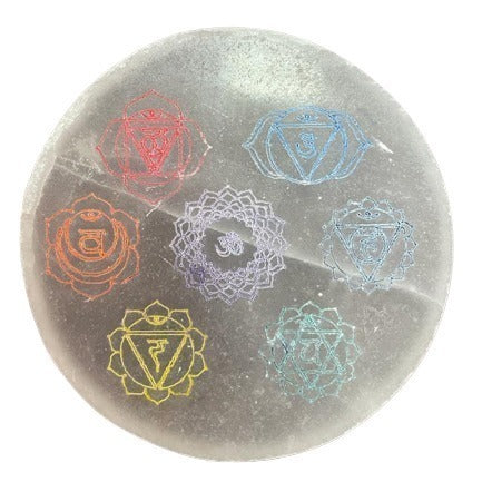 A circular, polished stone displays seven different colorful chakra symbols evenly spaced around its surface.