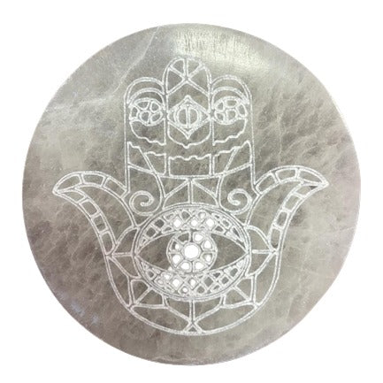 Hamsa, etched onto a round, flat, gray stone, faces forward with a central eye and detailed finger designs.