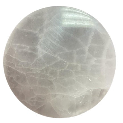 A smooth white stone orb with crack-like patterns rests against a stark white background. The orb’s surface reflects light, highlighting its rounded shape.