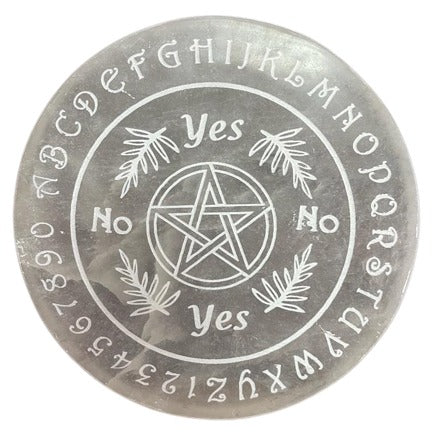 A gray, round spirit board features text, a pentagram, and fern illustrations. Inscribed text includes letters around the edge and "Yes" and "No" inside, surrounding a pentagram.