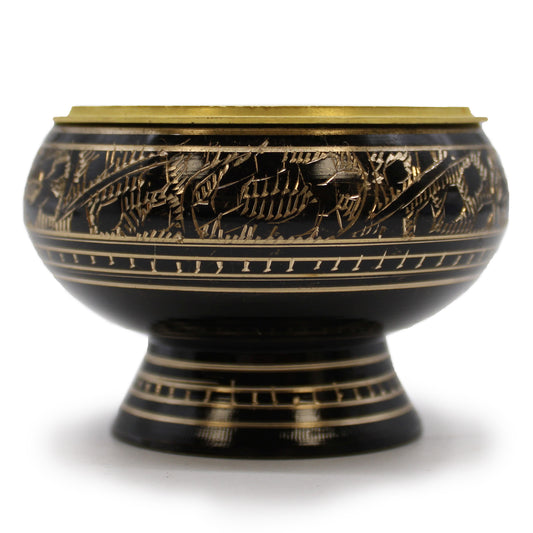 A black, intricately engraved bowl with gold floral patterns sits on a short pedestal base, set against a white background, highlighting its decorative craftsmanship and brass rim.