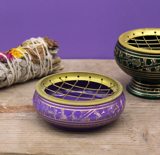 Purple incense burner with golden lattice design sits on wooden surface. Nearby, a sage bundle wrapped in string rests on the left, with a second burner partially visible to the right.