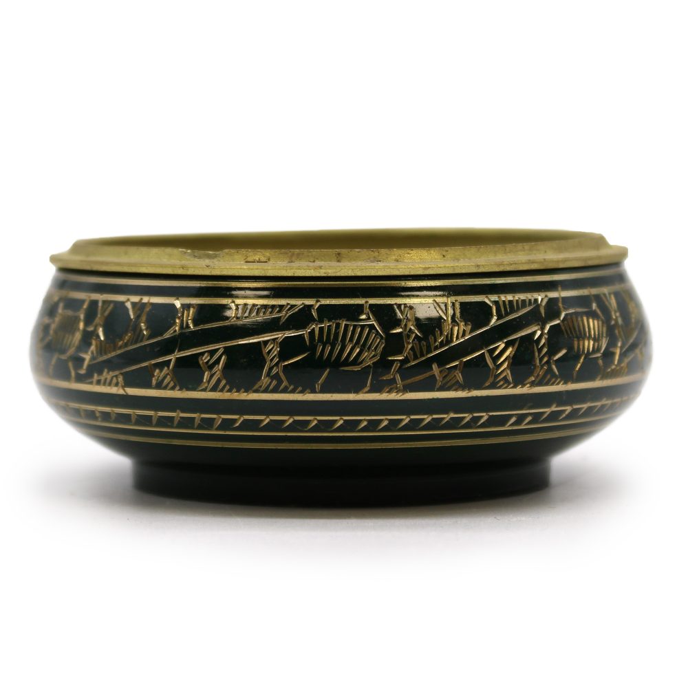 A decorative metal bowl features intricate, gold-colored engravings of figures and patterns along its dark band. It rests on a flat surface with a simple, elegant design.