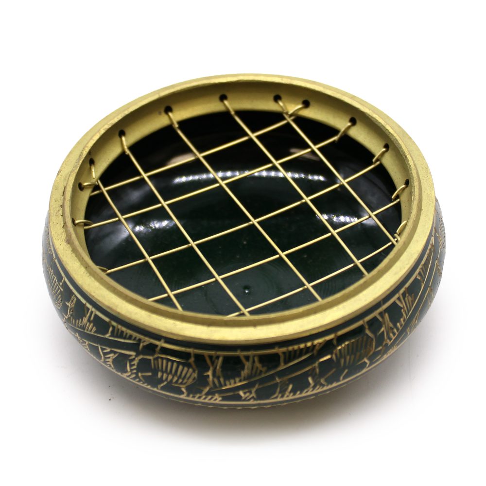 A round, decorative incense holder features a gold grid top and etched designs on the dark outer surface, sitting on a flat surface.