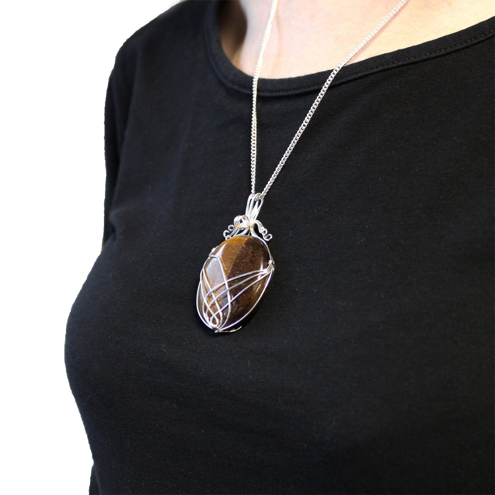 A large, brown tiger's eye pendant wrapped in silver wire hangs from a silver chain on a woman wearing a black shirt.