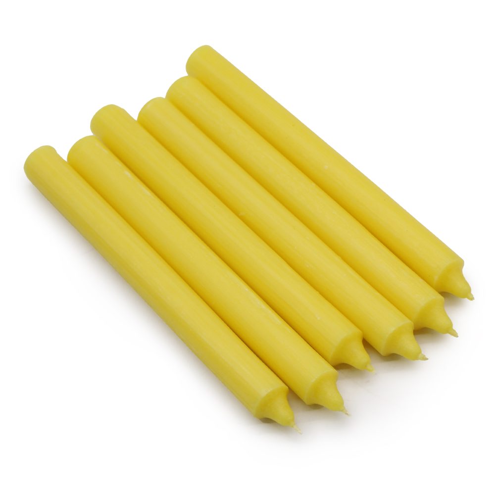 Seven yellow, unlit taper candles sit parallel, aligned diagonally on a white background.