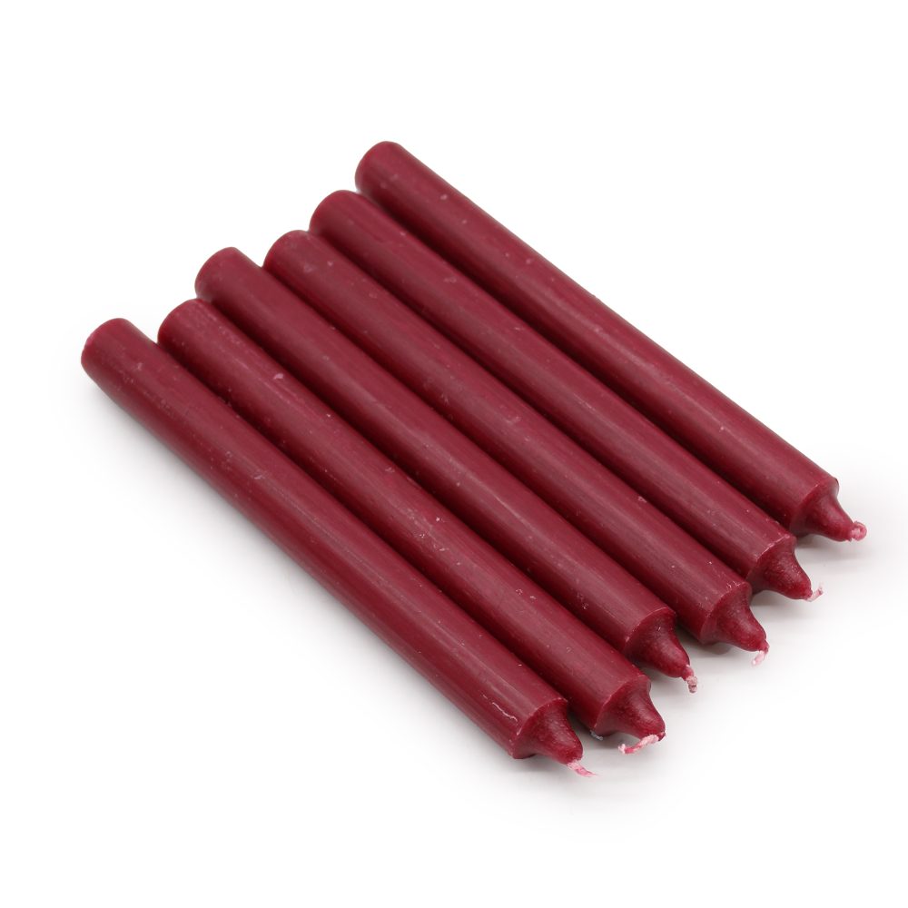 Six maroon-colored, unlit candles are lying parallel on a white surface. The candles are cylindrical with pointed tips.