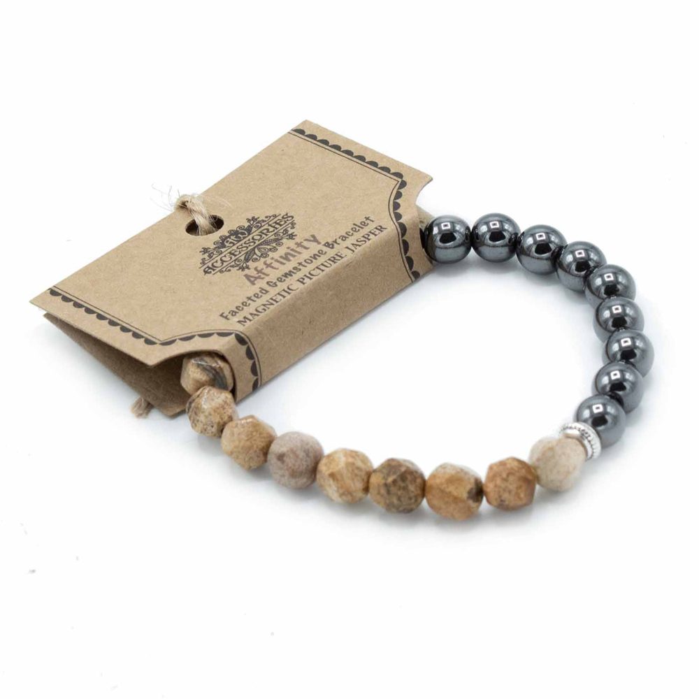 A beaded bracelet loops towards the viewer, with one end connected to a brown tag reading "ACCESSORIES Affinity Faceted Gemstone Bracelet MAGNETIC PICTURE JASPER", resting on a white surface.