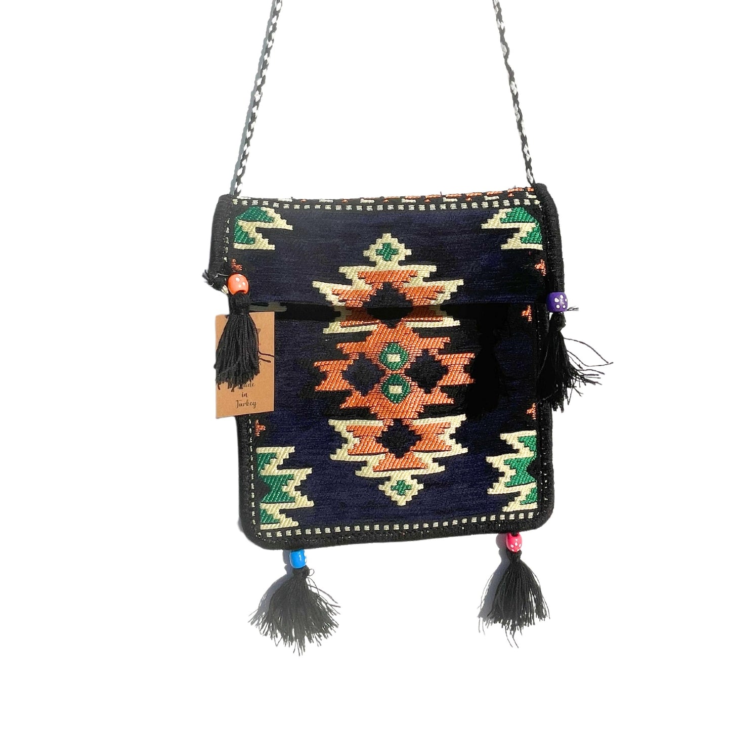 The woven shoulder bag, detailed with colorful geometric patterns and tassels, hangs by a silver chain. The bag is isolated on a white background, and it has a tag that reads "Made in Turkey."