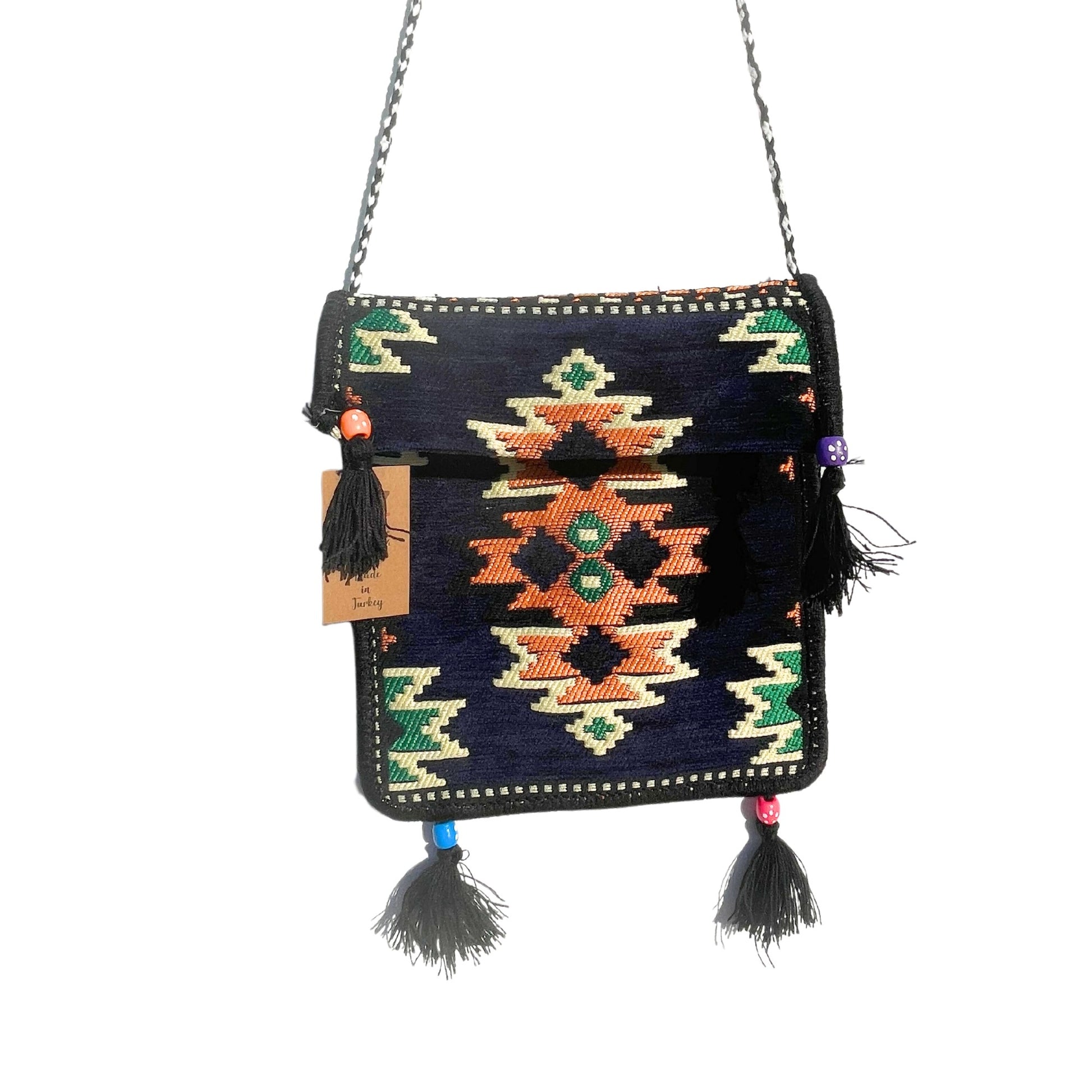 The woven shoulder bag, detailed with colorful geometric patterns and tassels, hangs by a silver chain. The bag is isolated on a white background, and it has a tag that reads "Made in Turkey."