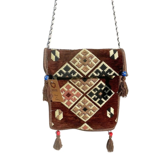 A patterned brown bag hangs, displaying diamond designs in black, cream, and pink hues. It has tassels, beads, and a tag that reads: "ANCIENT WISDOM. Made in Turkey". The background is white.
