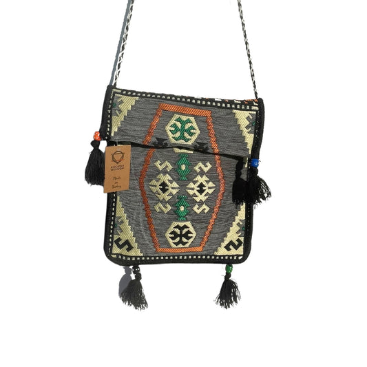 A woven bag hangs, decorated with gray, orange, green, and beige patterns. The bag has tassels at the bottom corners. A tag reads "ANCIENT WISDOM, Made in Turkey".