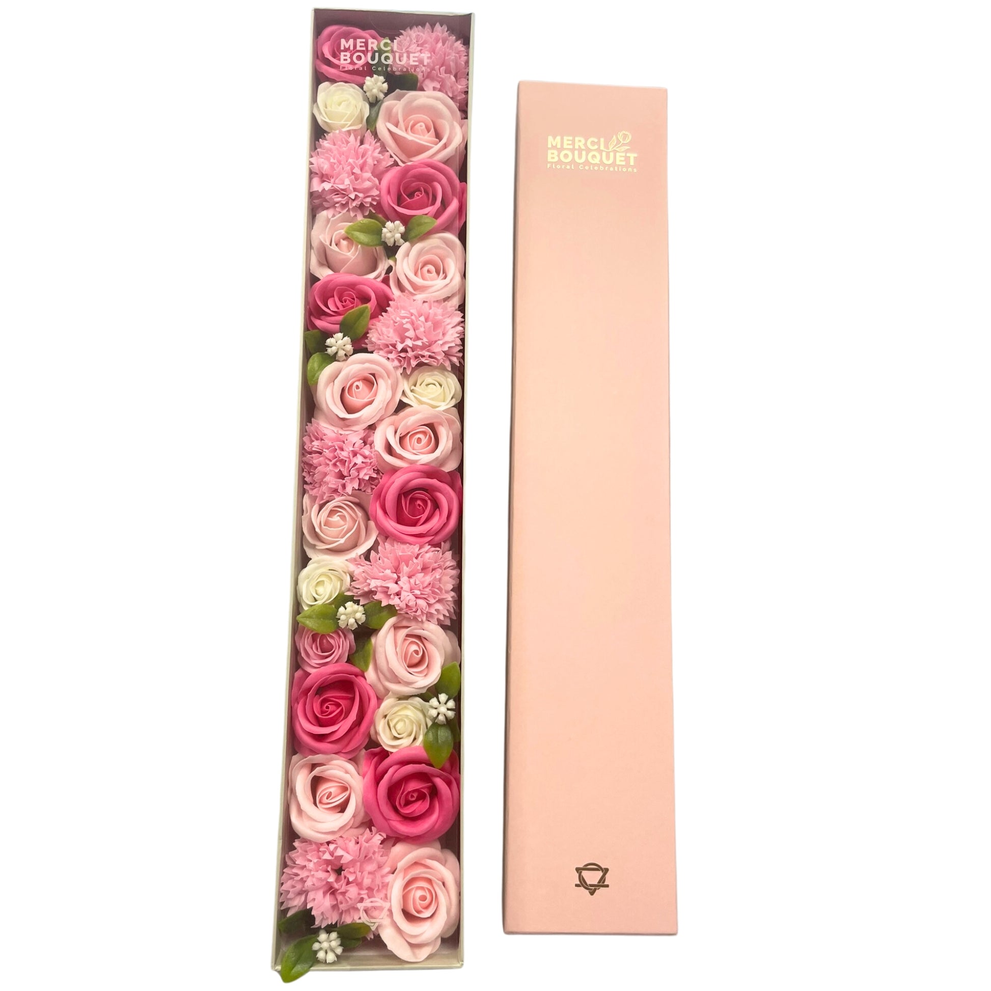 A long box containing a pink and white soap flower arrangement sits next to its matching lid.  MERCI BOUQUET Floral Celebrations is printed on both the box and its lid.