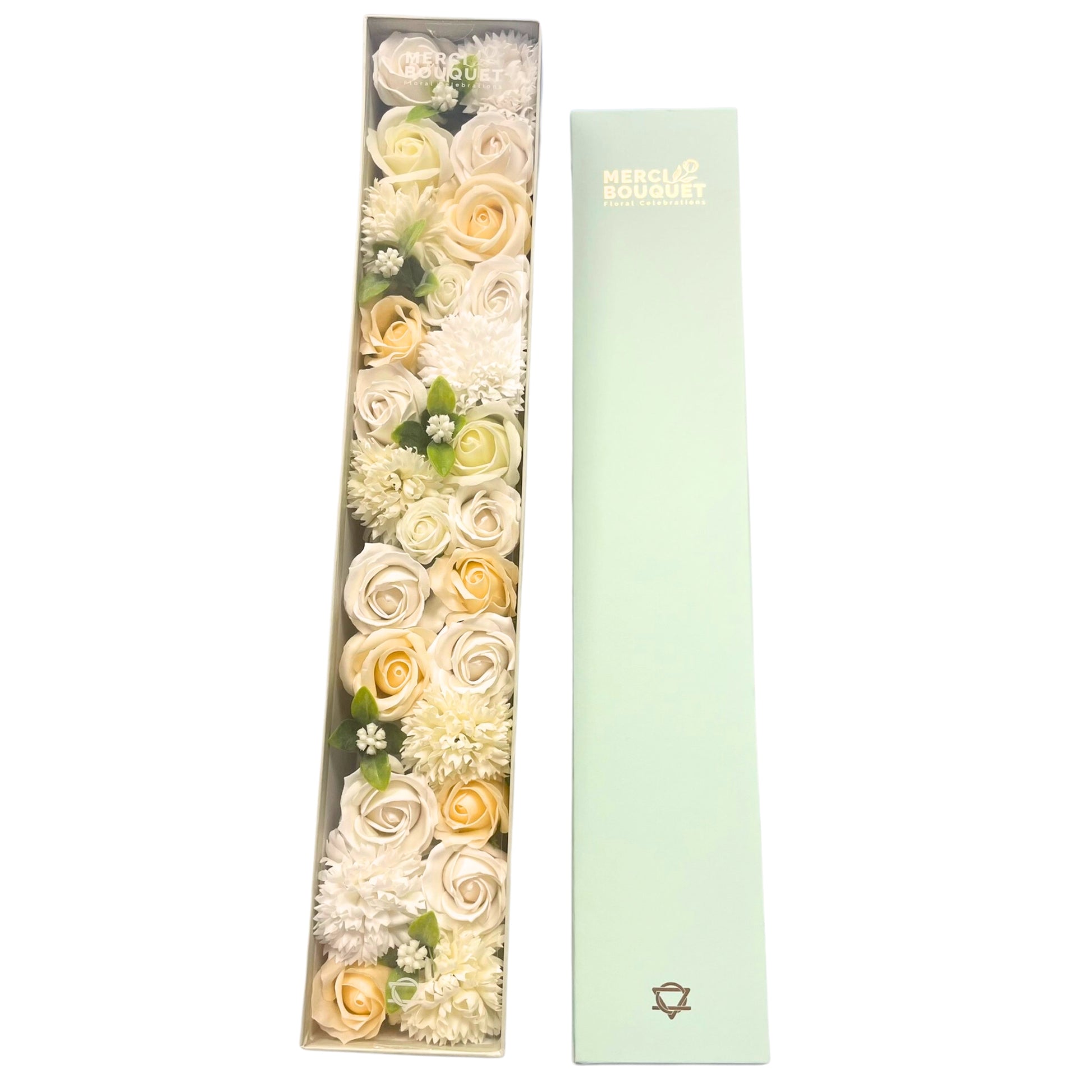 A long rectangular box contains an arrangement of artificial white and cream roses and chrysanthemums.  The box is partially open next to its pale green cover. MERCY BOUQUET Floral Celebrations is printed on both the box and its cover.