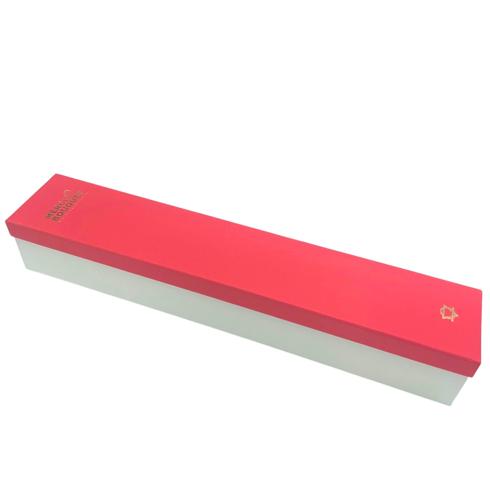 A long, rectangular box, rests on a white background.  The top is bright pink; the bottom is off-white.  It's labeled "MERCI BOUQUET" in gold lettering.