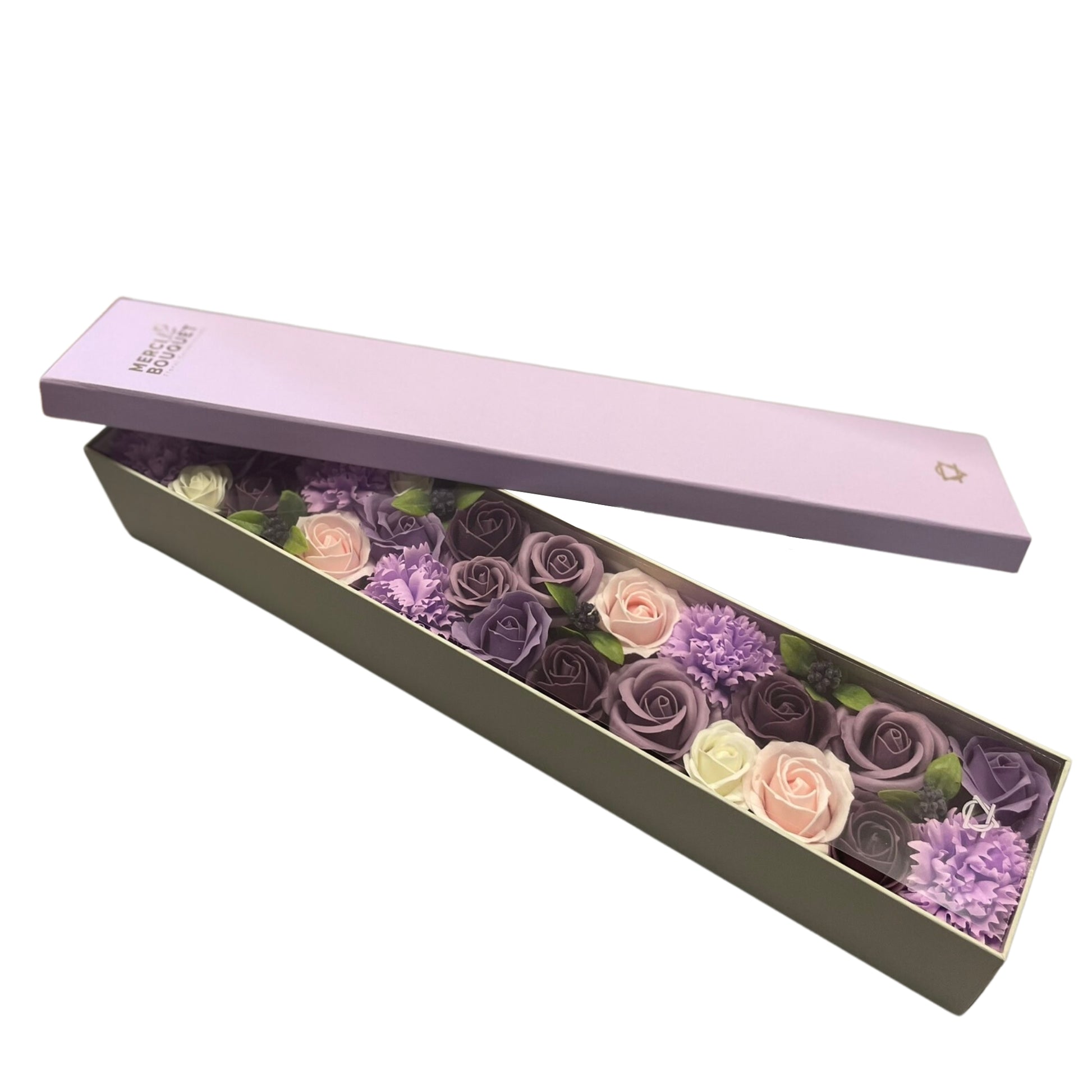 A long box containing a bouquet of purple and pink soap roses and carnations rests on a white background.  The lid, a light purple, is ajar.  The box is labeled: MERCI BOUQUET.