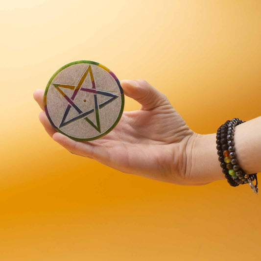 A hand holds a circular wooden disc displaying a colorful star design, against a warm, orange background. The wrist is adorned with beaded bracelets.