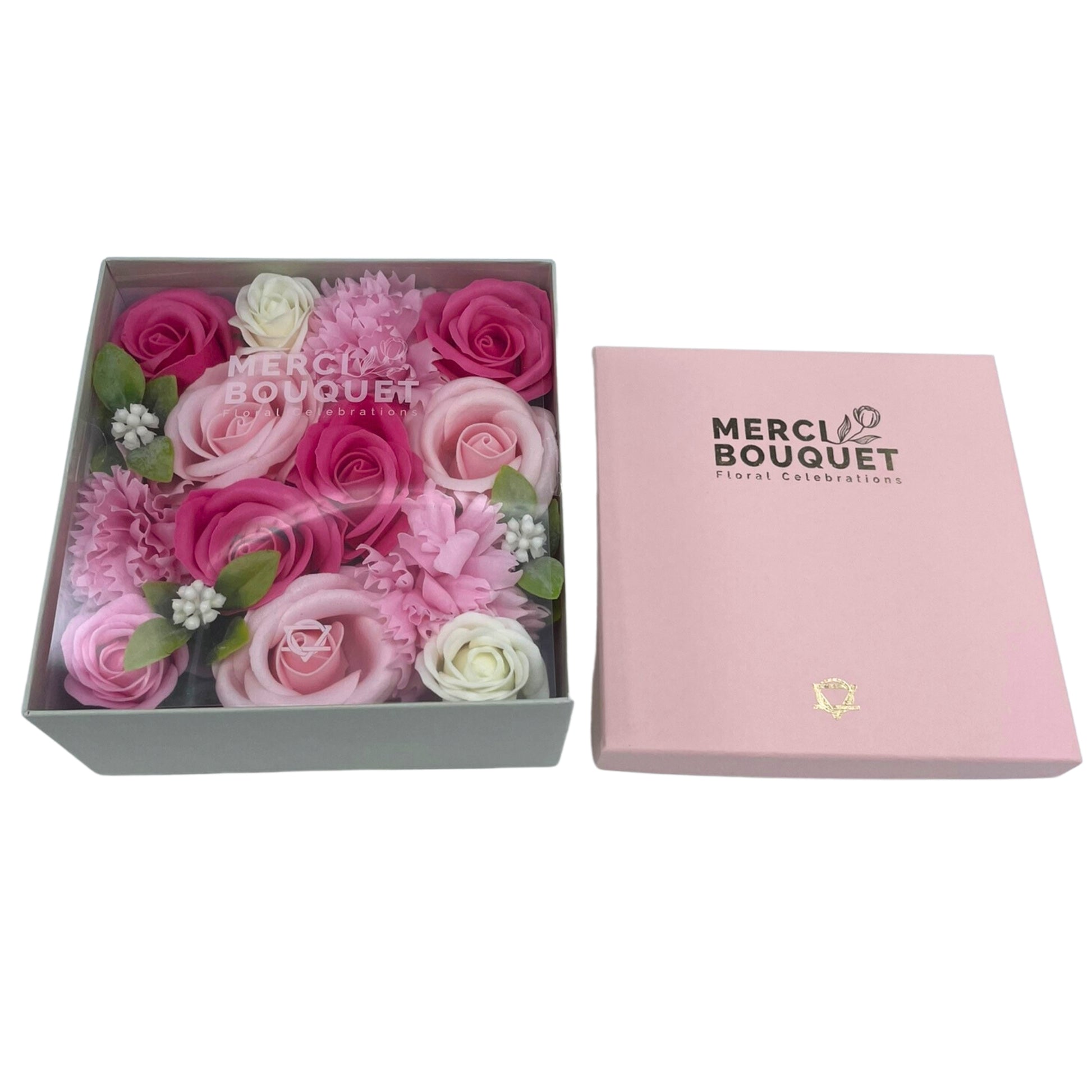 A box of pink and white soap flowers sits atop a light grey box.  The flowers are arranged in a square shape.  The larger box is pink and says "MERCI BOUQUET Floral Celebrations" on it.