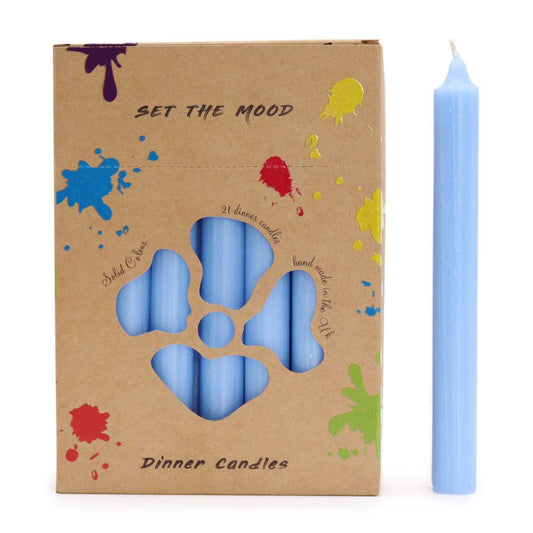 A box of "SET THE MOOD" dinner candles sits beside a single candle. The box is kraft colored with paint splatter designs and a cut-out revealing light-blue candles inside. The text reads: "SET THE MOOD, Solid Colour, 21 dinner candle, hand made in the Uk, Dinner Candles".