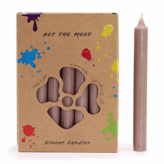 A box of taupe candles features a flower-shaped cutout showcasing the candles within. One candle stands beside the box. The box reads "SET THE MOOD," "Solid Colour," "21 dinner candles," "hand made in the UK," and "Dinner Candles". The box is decorated with bright paint splatters.