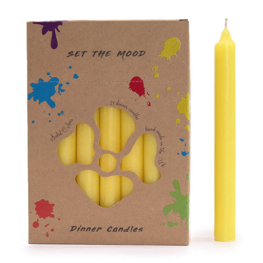 A box of yellow dinner candles labeled "SET THE MOOD" and "Dinner Candles" has a flower-shaped cutout displaying multiple candles. Splatters of colorful paint decorate the box. A single candle stands beside it.