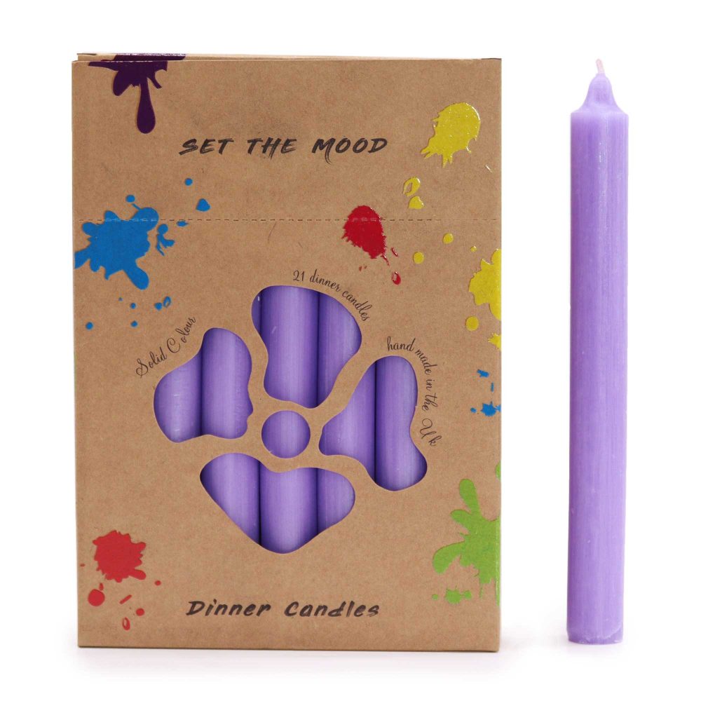 A box of lavender dinner candles, with the label “SET THE MOOD” and “Dinner Candles” on brown paper, and color splashes, sits alongside a single, lavender, lit candle. The box says, “21 dinner candles”, “Solid Colour” and “Hand made in the UK”.