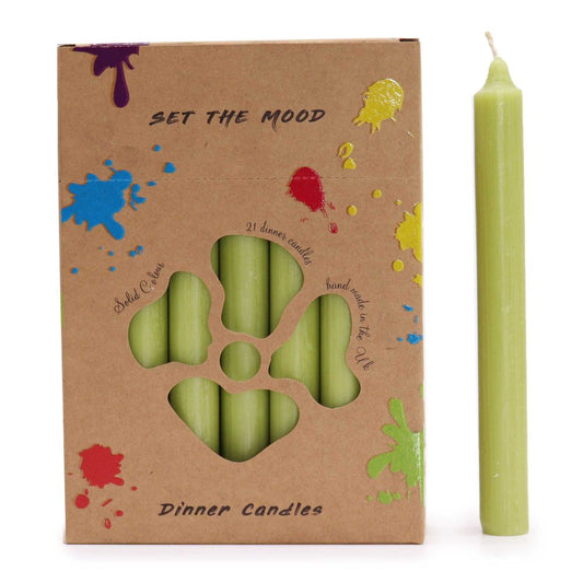 A box of green taper candles sits next to a single candle, “SET THE MOOD,” “Solid Colour,” “21 dinner candles,” “hand made in the UK” and “Dinner Candles” are printed on the brown cardboard box decorated with colorful splatters.