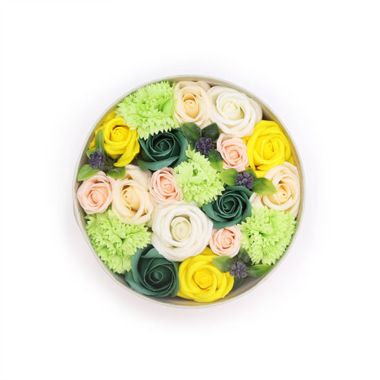 Soap flowers of various pastel colors and greens are arranged in a circular box.