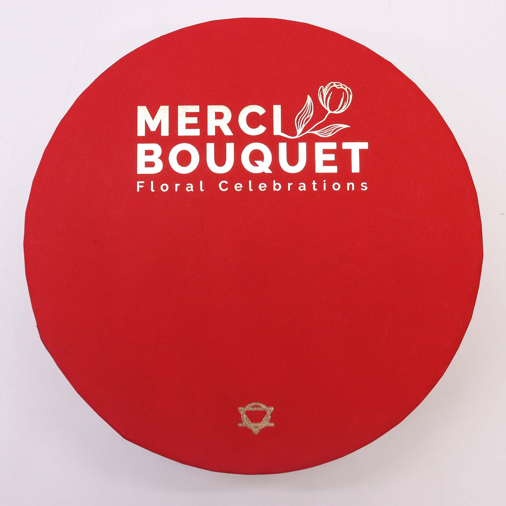 A red, circular box displays "MERCI BOUQUET Floral Celebrations" in gold and white lettering.  A small gold symbol is at the bottom.